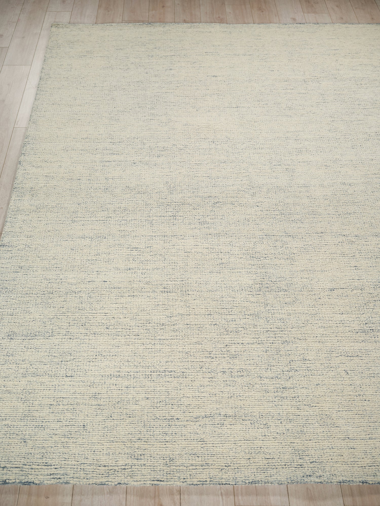Cream textured area rug with subtle blue-gray linear pattern on light wood floor.