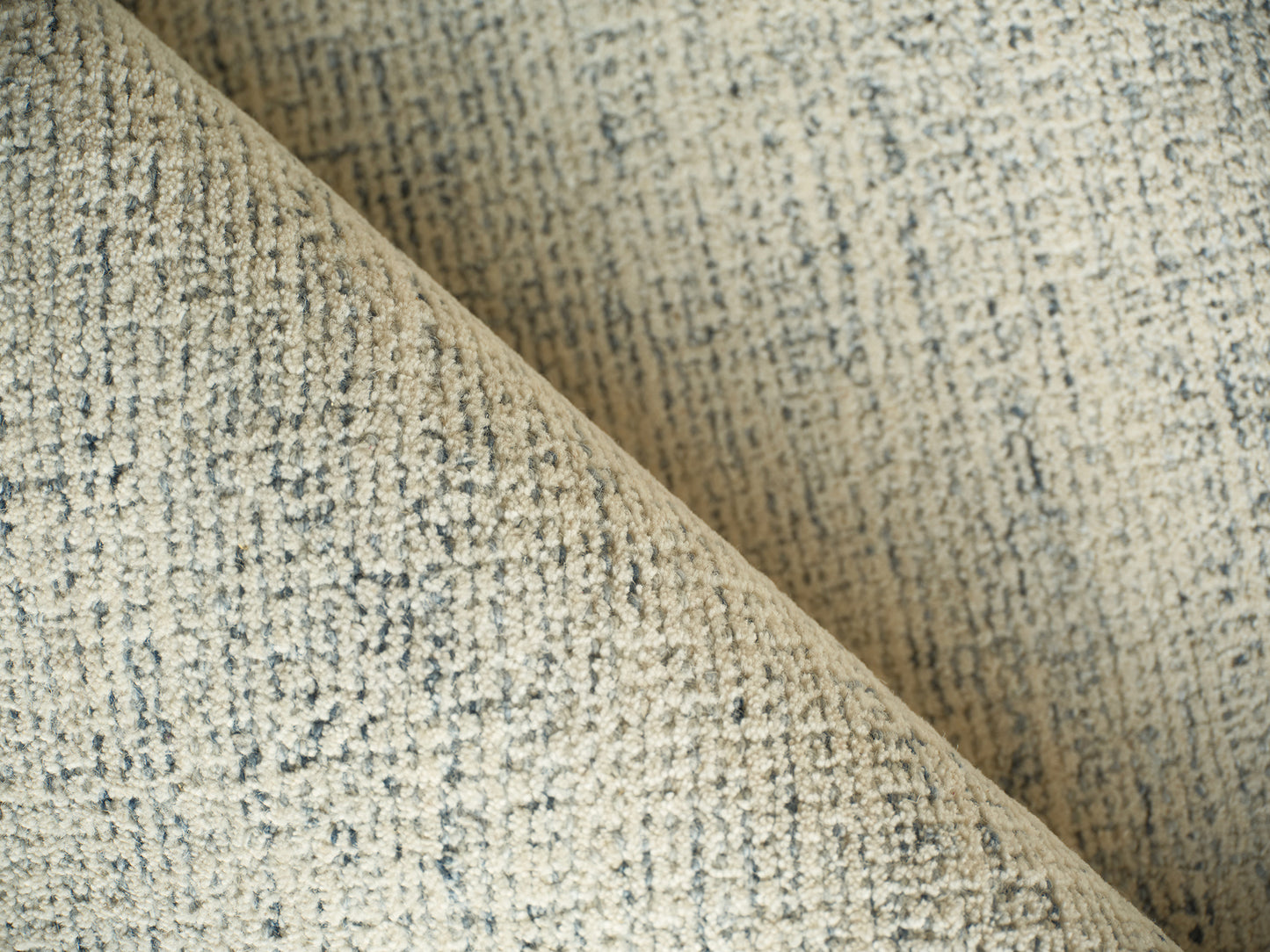 Beige rug with a tweed-like woven texture and blue-gray flecks, folded to show the surface; indoor hand-tufted, 2' x 3'.