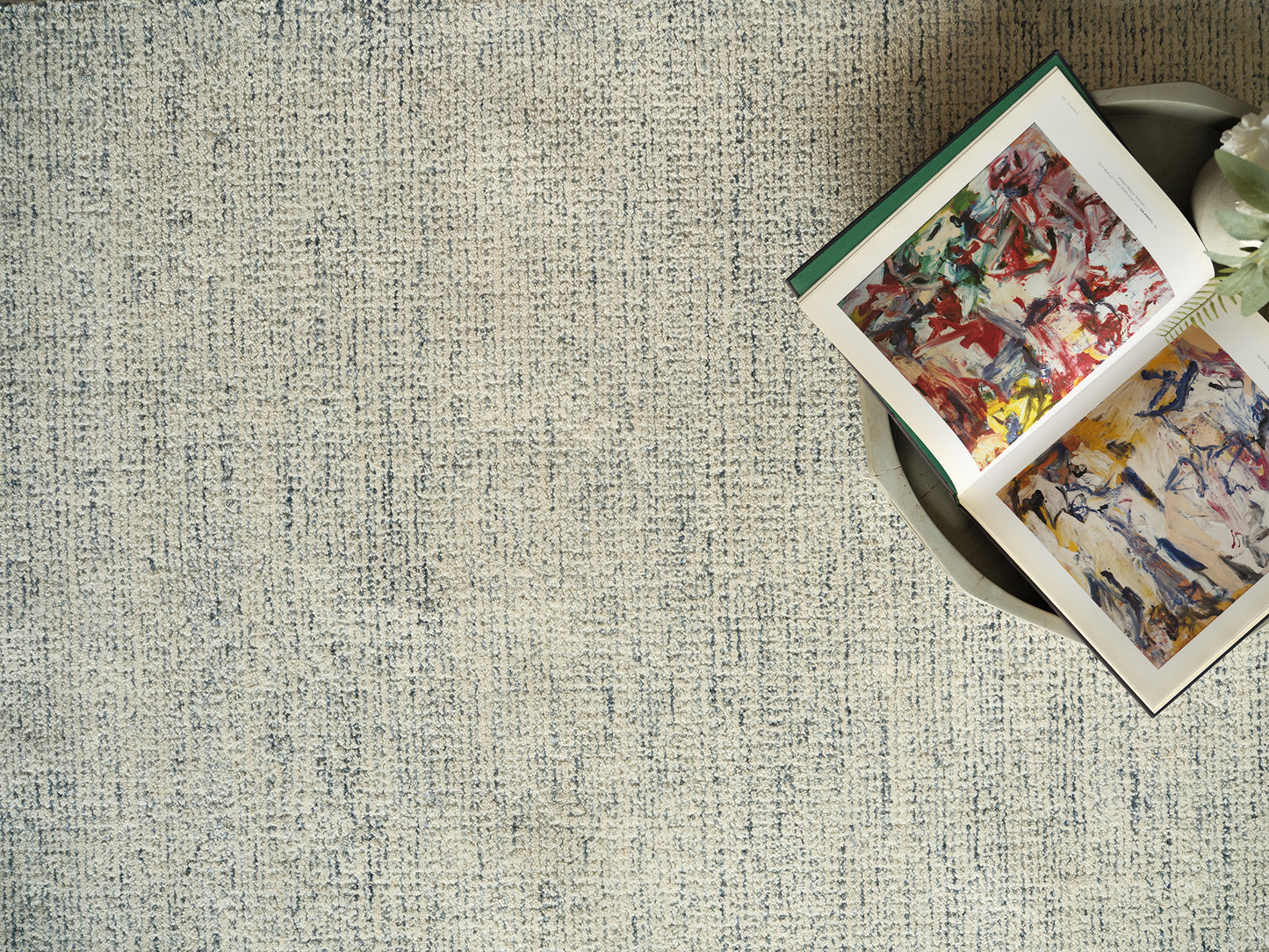 Beige textured rug with an open colorful abstract art book resting on a round tray.