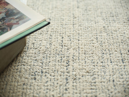 Beige textured rug with a soft loop pile; magazines stacked on a wooden box at the left.