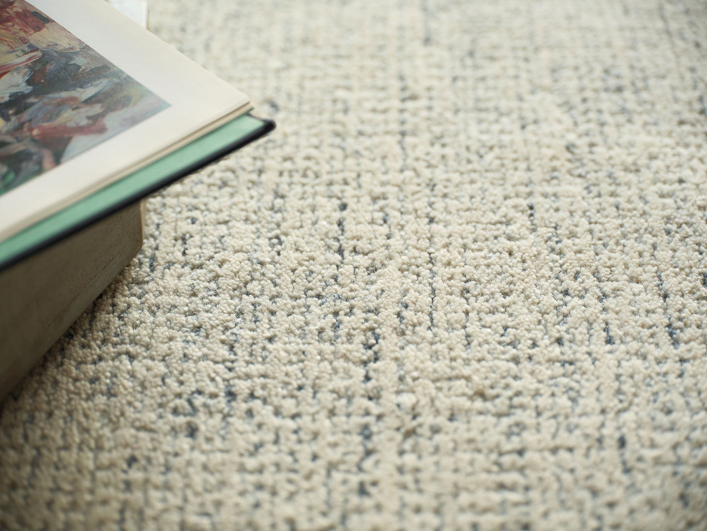 Beige textured loop-pile rug with a partially open book showing colorful artwork resting along its edge.