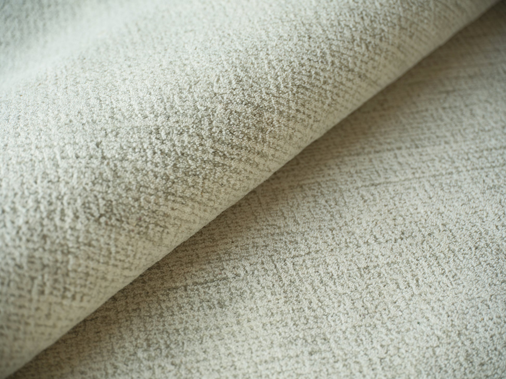 Close-up of pale beige indoor hand-tufted rug with plush looped texture and folded edge.