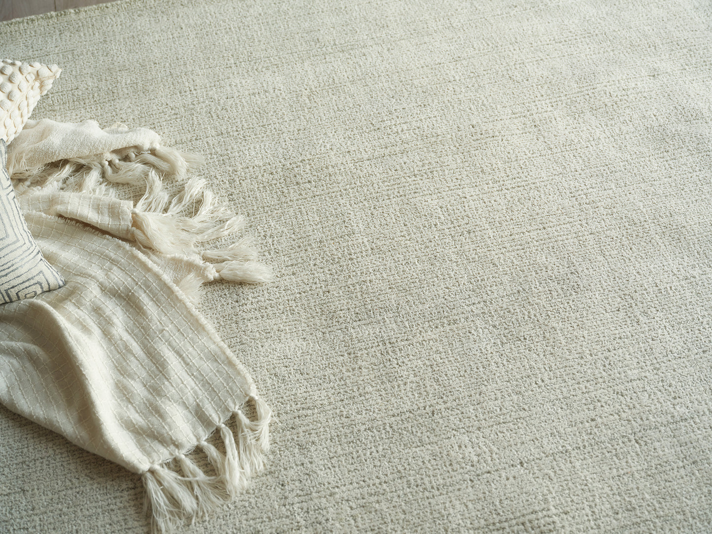 Cream woven rug with a fringed beige throw blanket and a striped pillow on the left, cozy neutral living room look.