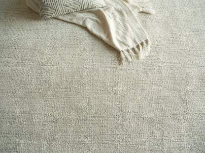 Beige textured rug with cream fringed throw and geometric-patterned pillow.