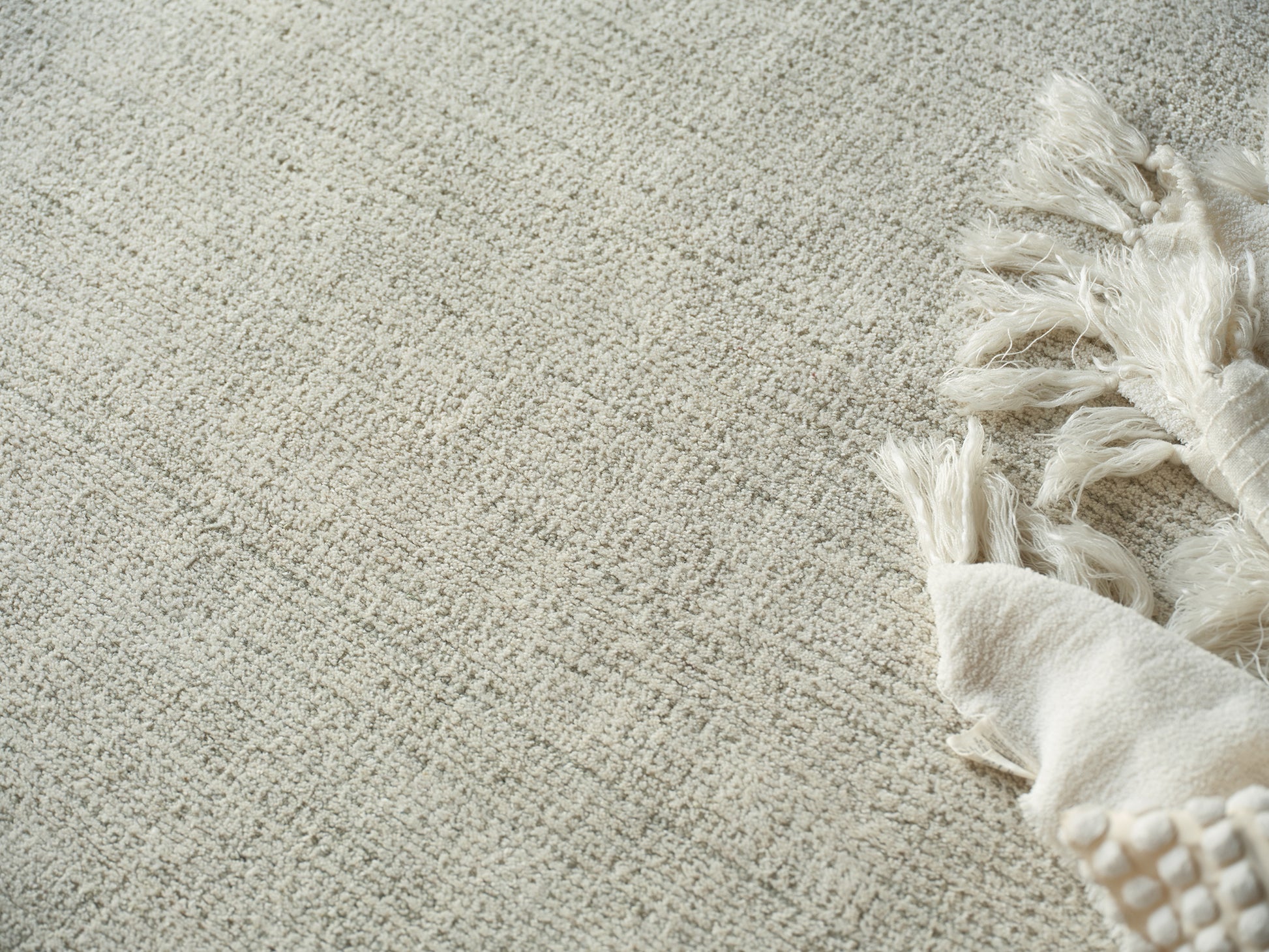 Beige textured rug with chunky cream fringe along the right edge and a light throw draped beside.