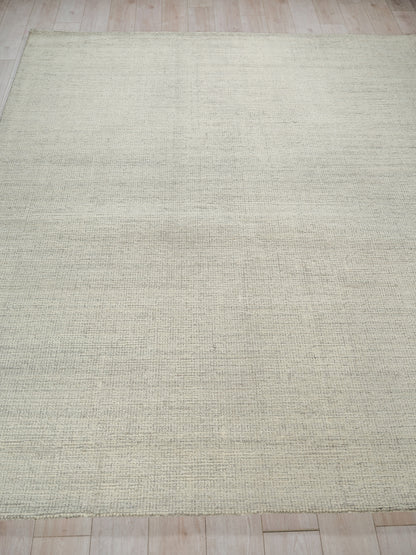 Beige hand-tufted rug with a subtle textured pattern on light wood floor, 6' x 9'.