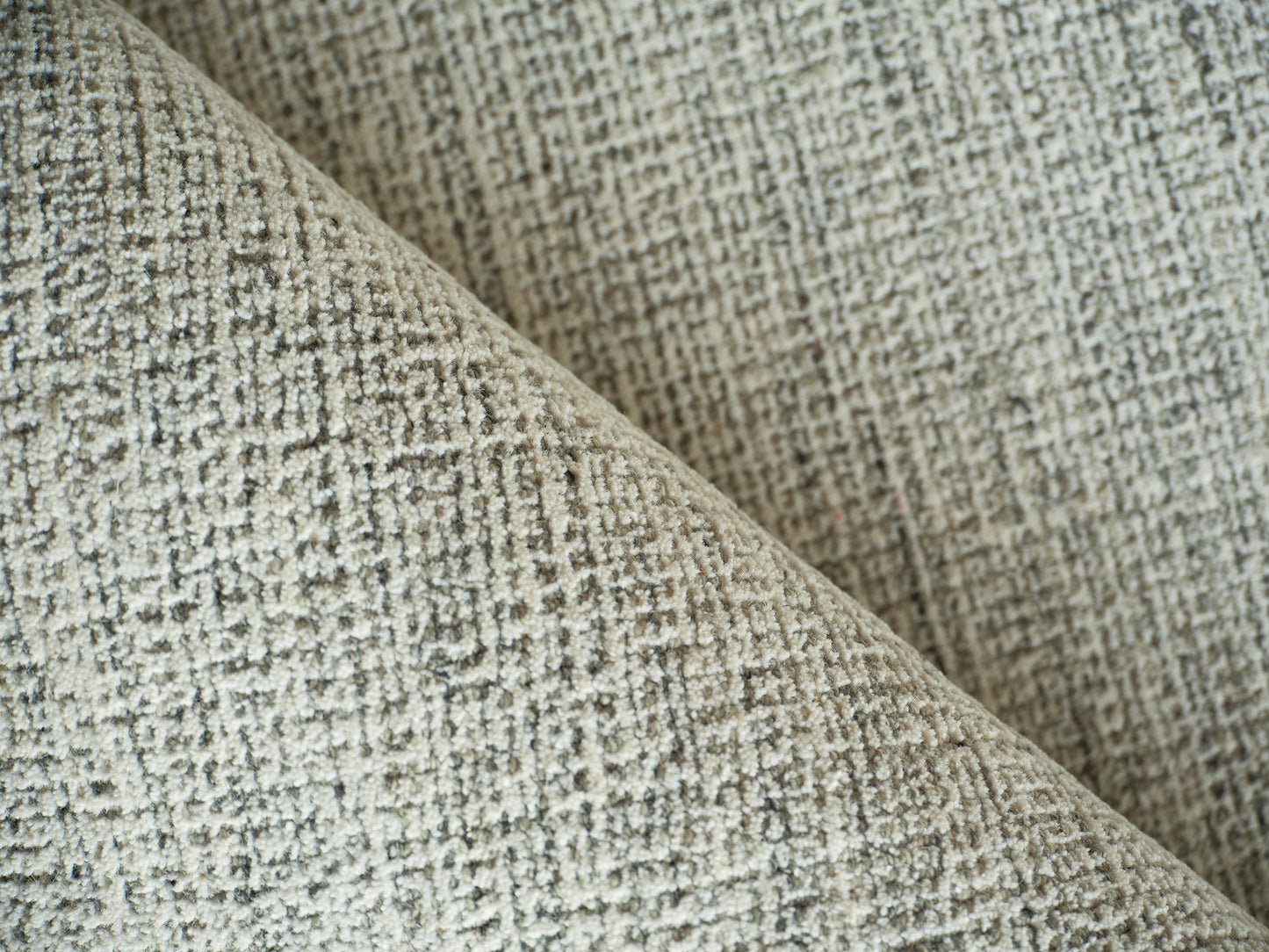 Beige textured woven rug with a subtle grid pattern, folded to reveal a soft, plush pile.