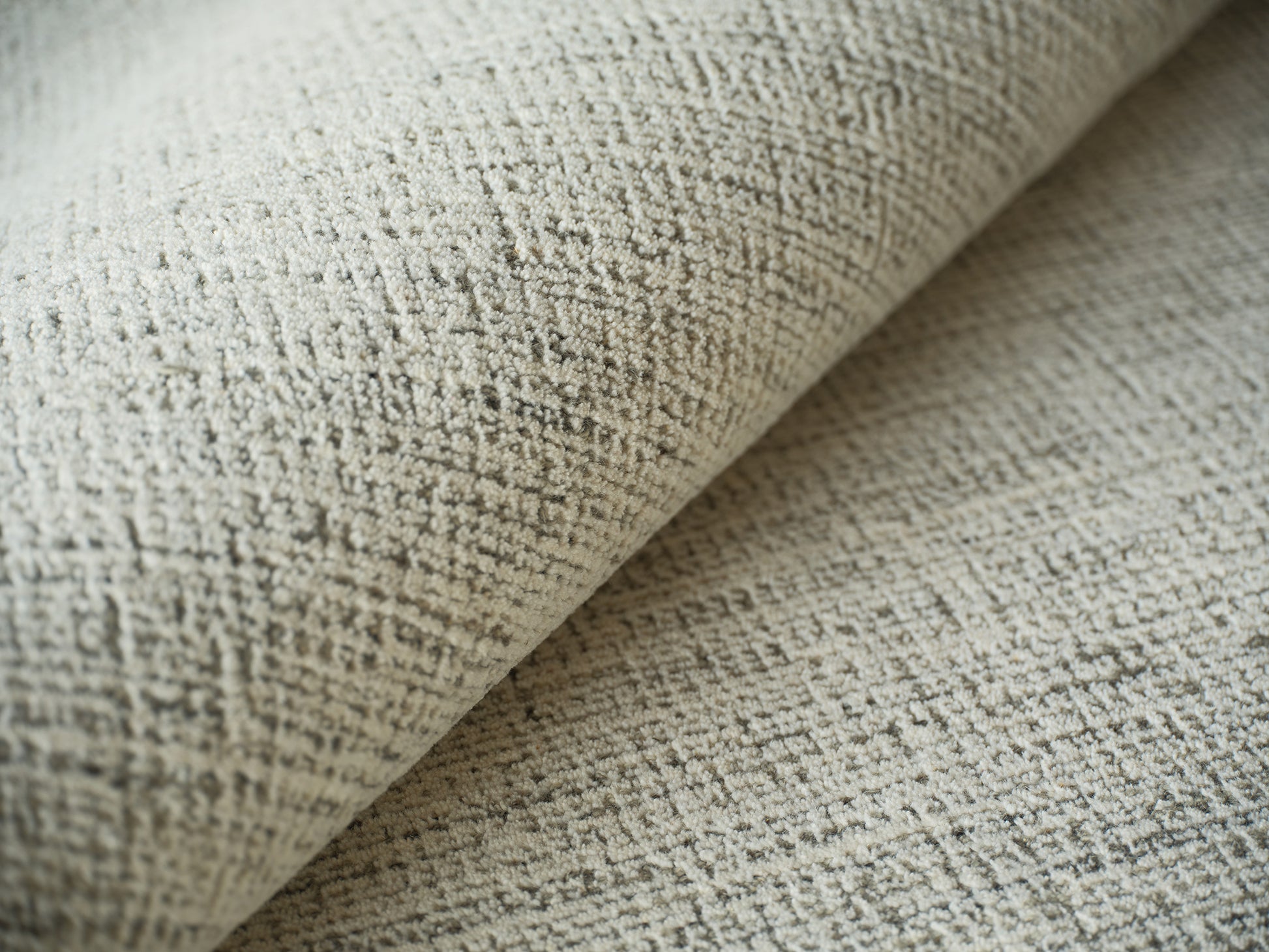 Close-up of neutral beige textured rug with a looped hand-tufted weave and rolled edge.