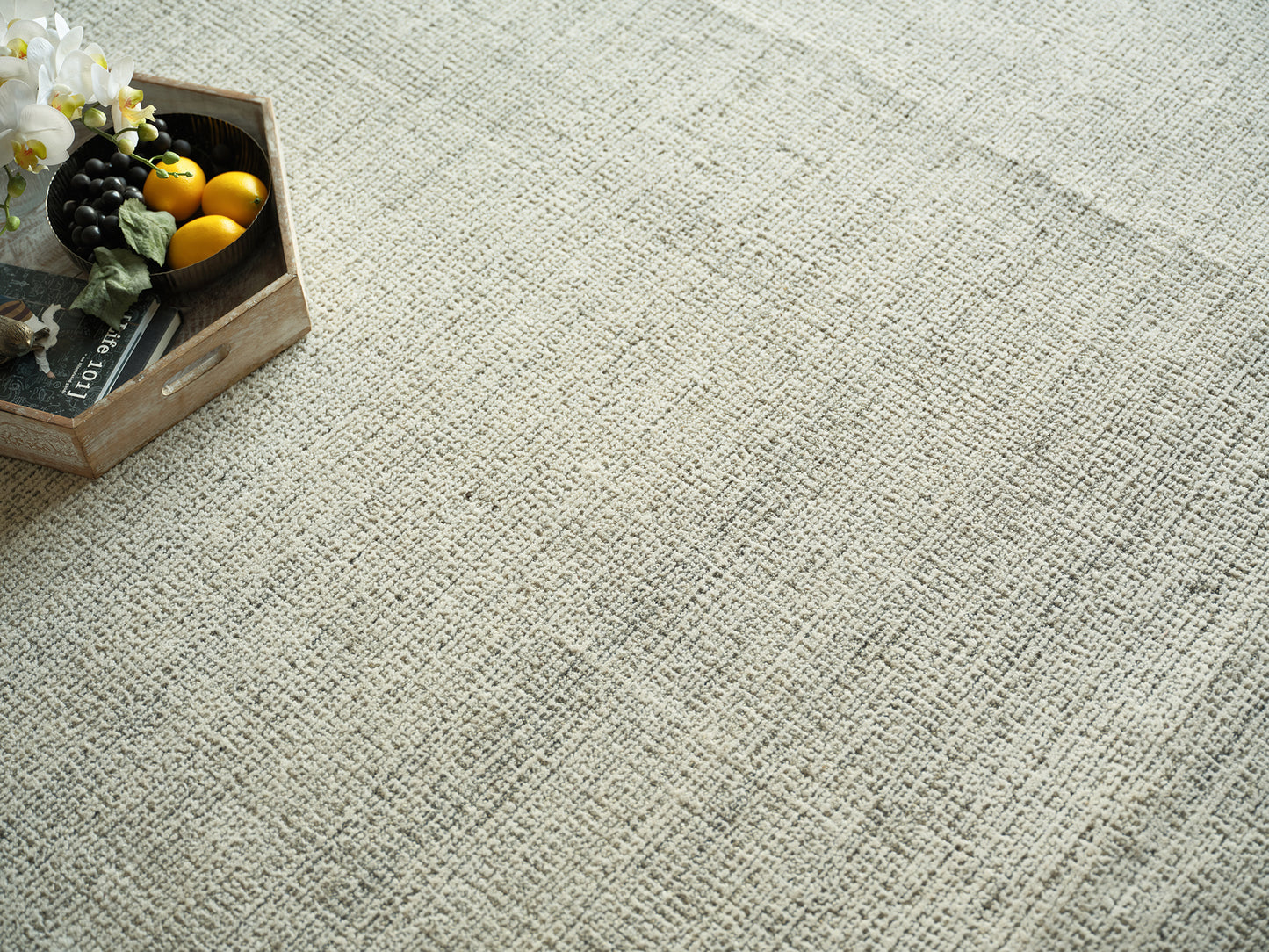 Beige textured rug with a rustic wooden crate holding yellow lemons, black grapes, and white orchids on the left.