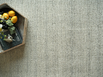 Wooden crate with yellow citrus, dark grapes, greenery, a small bird figurine and a book on a beige textured rug.