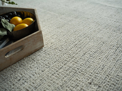 Rustic wooden crate with a round black tray holding bright yellow lemons and dark grapes on a beige textured rug