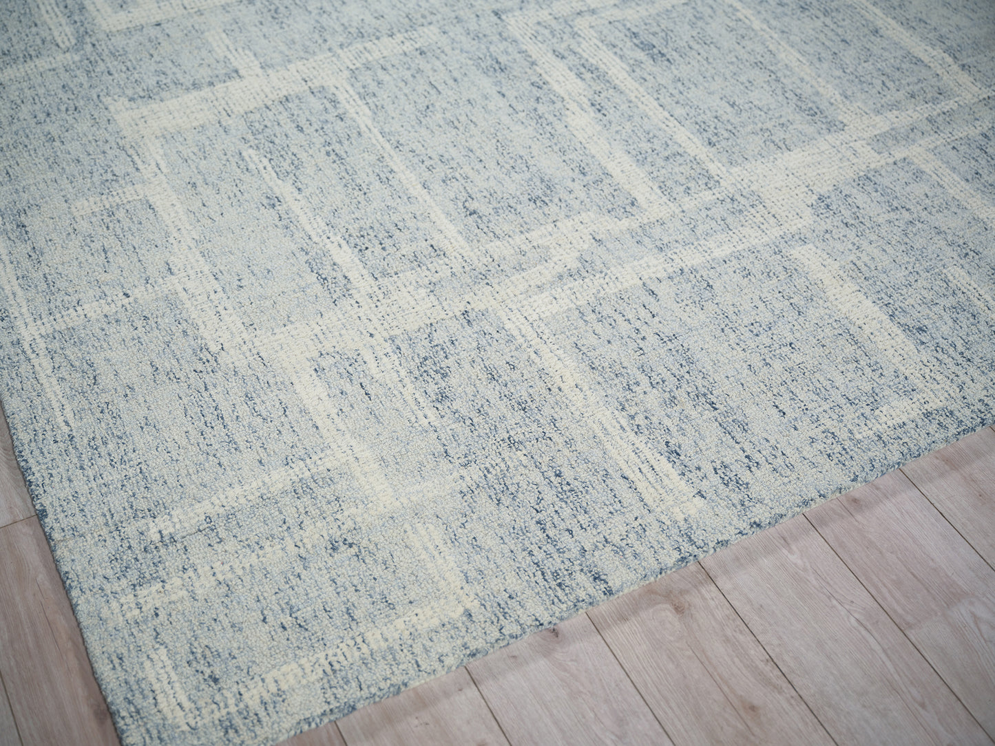 Blue-gray area rug with ivory distressed geometric pattern on light wood floor.