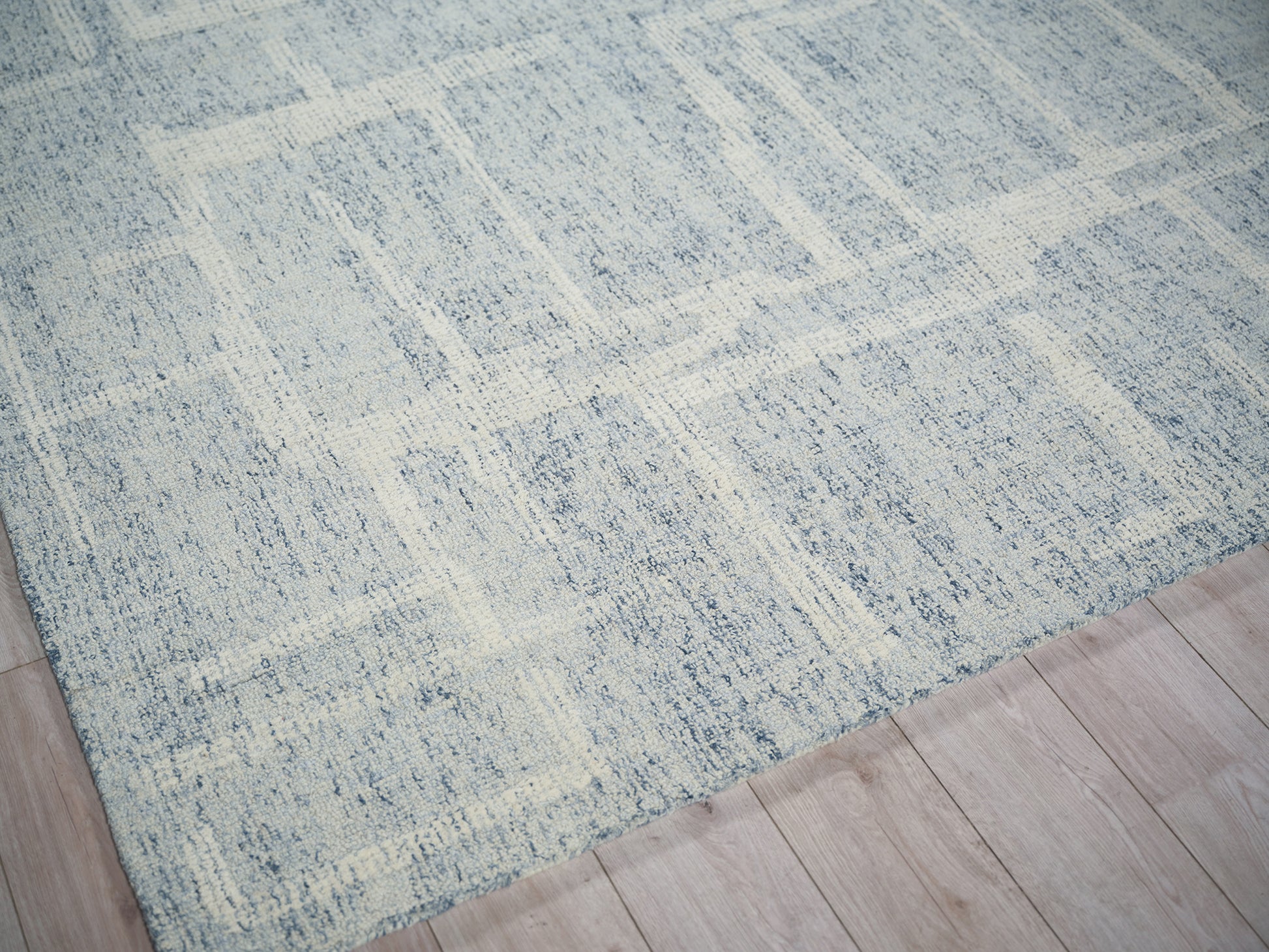 Blue-gray area rug with ivory distressed geometric pattern on light wood floor.