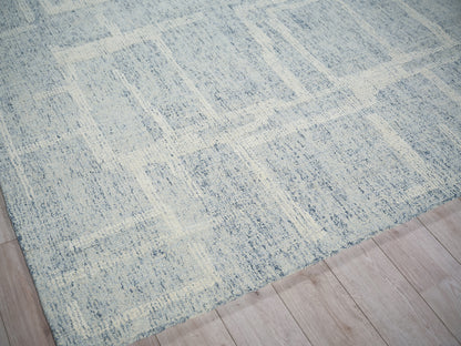 Blue-gray area rug with ivory distressed geometric pattern on light wood floor.