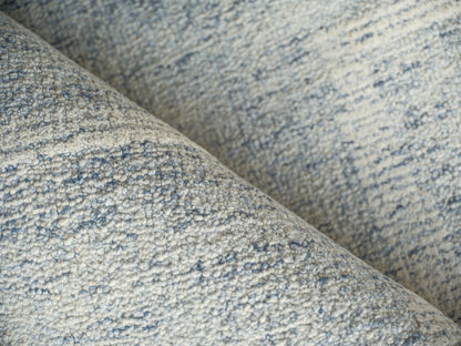 Close-up of a light blue-gray boucle rug with speckled heather texture and soft loop pile.
