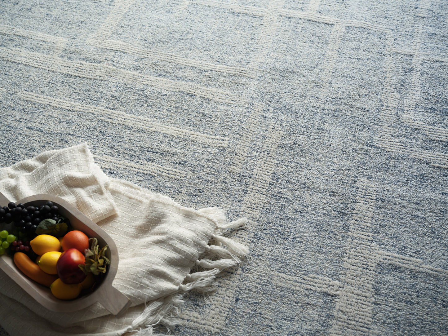 Wooden tray on white fringed cloth with colorful grapes, peppers and an apple on a pale blue patterned rug.