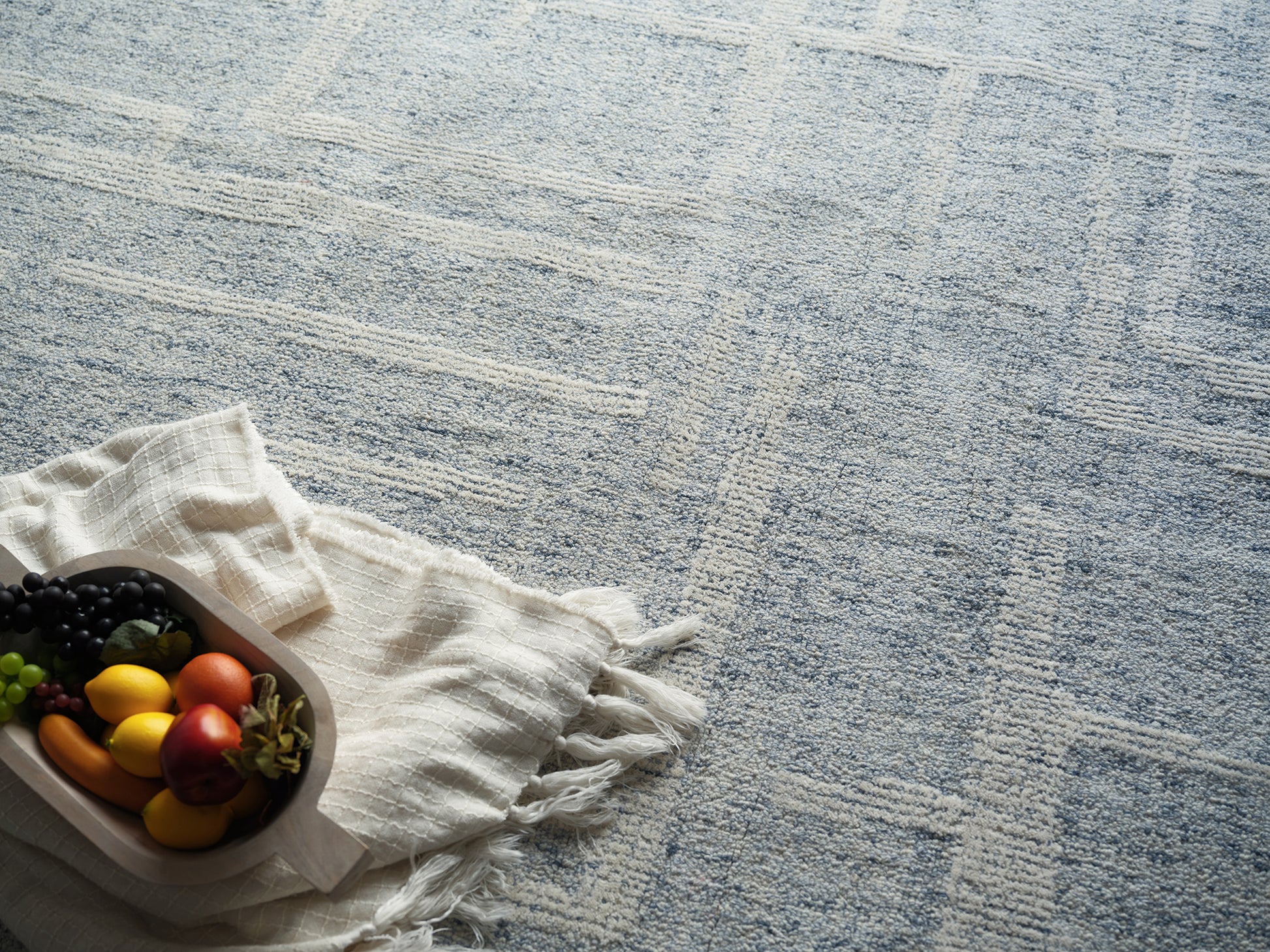 Wooden tray on white fringed cloth with colorful grapes, peppers and an apple on a pale blue patterned rug.