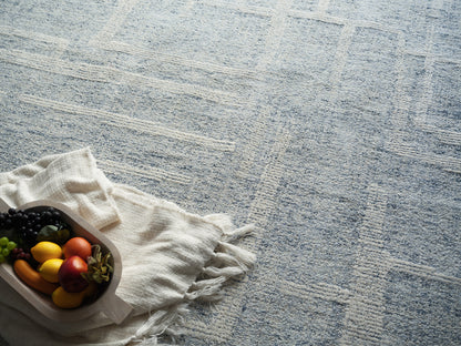 Wooden tray on white fringed cloth with colorful grapes, peppers and an apple on a pale blue patterned rug.