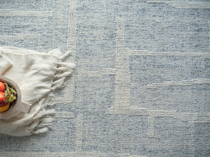 Blue textured rug with cream fringed throw and small wooden bowl of red and yellow peppers.