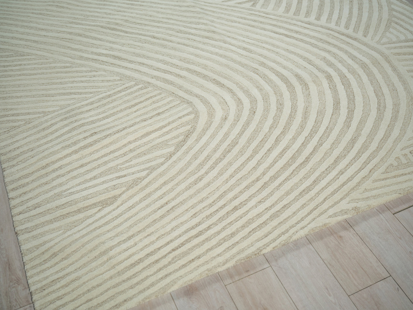 Beige rug with cream wavy stripes forming curved geometric pattern on a light wood floor.