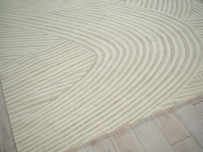 Beige rug with cream wavy stripes forming curved geometric pattern on a light wood floor.