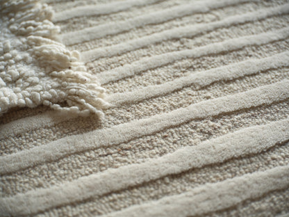 Beige textured rug with ribbed stripes and a cream fluffy fringe along the edge.