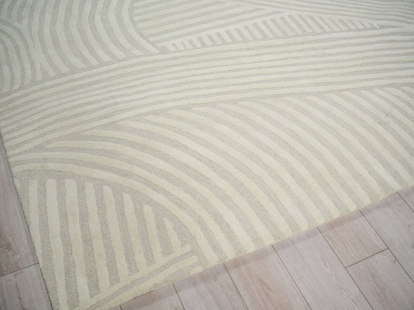 Cream rug with taupe curved stripe pattern on light wood floor.