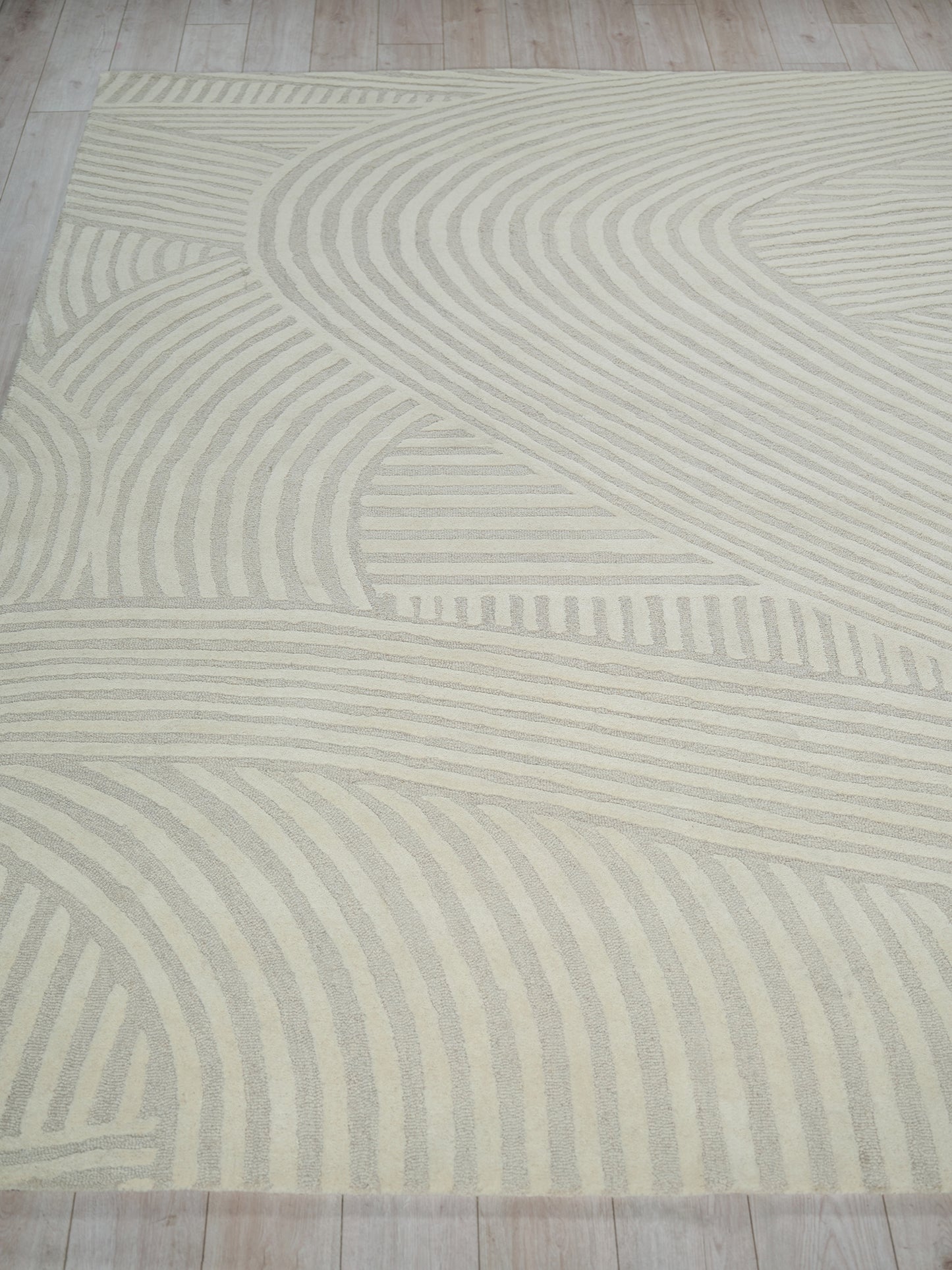 Cream area rug with light beige wavy stripes forming an abstract geometric pattern.