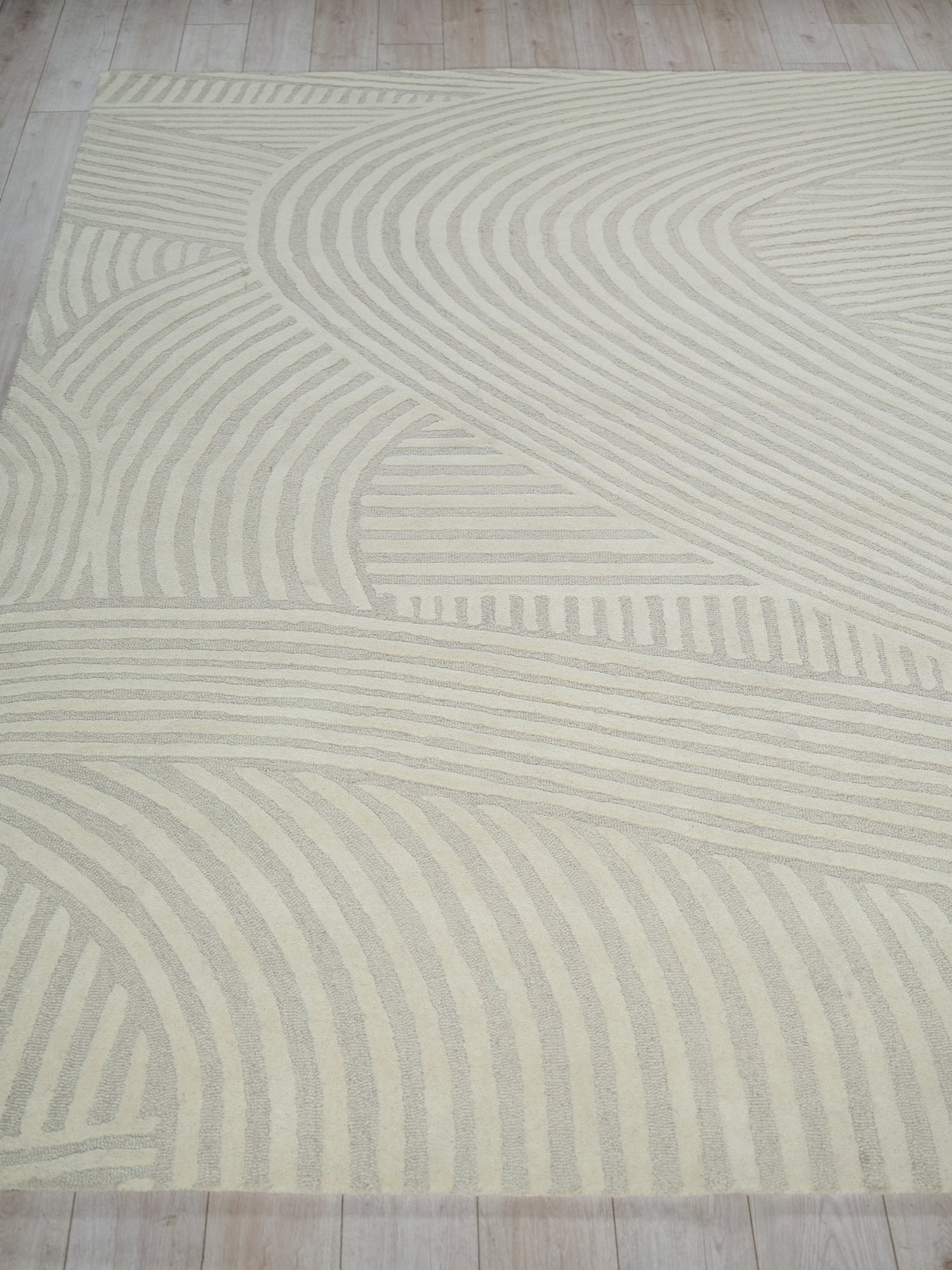 Cream area rug with light beige wavy stripes forming an abstract geometric pattern.
