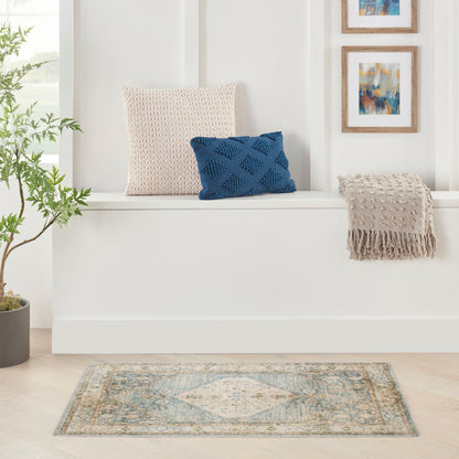 White window seat with beige knit pillow, blue diamond-knit pillow, beige fringe throw, plant, framed art, blue-gray rug.