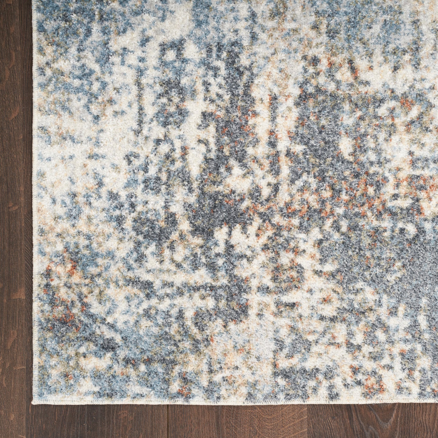 Abstract blue-gray rug with ivory and rust accents on dark wooden floor.