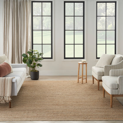 Neutral living room with black-framed windows, beige sofa, matching armchairs, jute rug, potted plant, light curtains.
