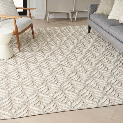 Beige textured tropical 9' x 12' area rug with a raised leaf motif in a neutral living room; gray sofa, wooden-armchair, and light wood flooring.