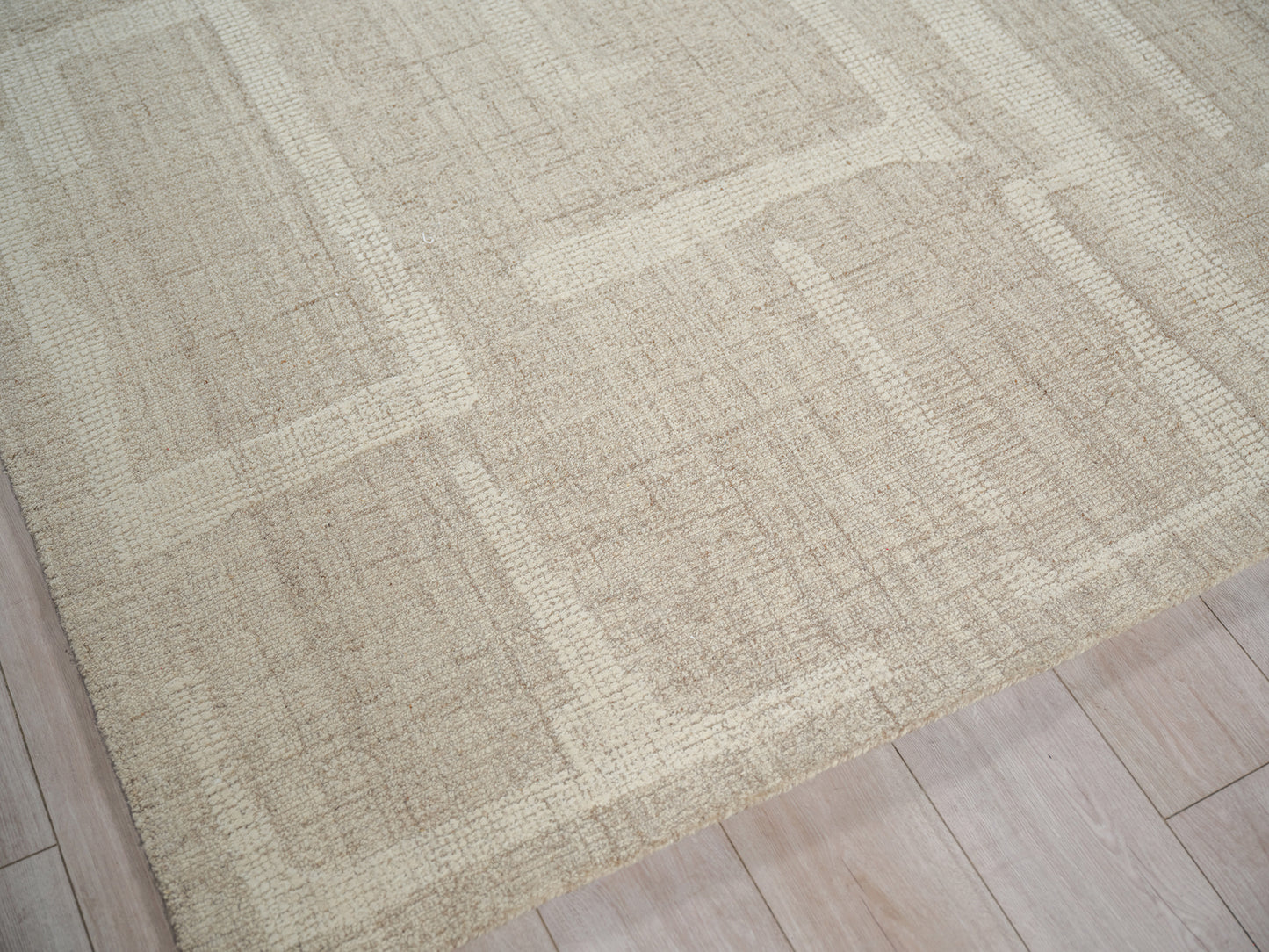 Beige rectangular hand-tufted rug with subtle cream and tan geometric blocks on light wood floor.