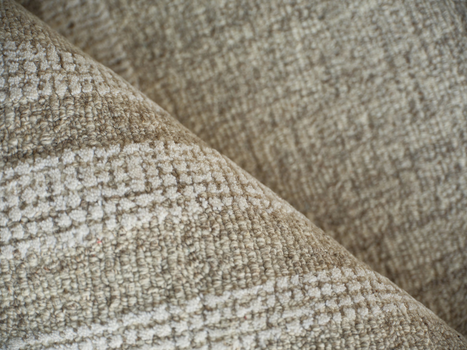 Beige textured woven rug with a boucle-like surface, close-up of a folded edge.
