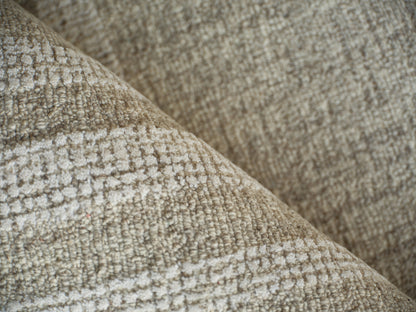 Beige textured woven rug with a boucle-like surface, close-up of a folded edge.