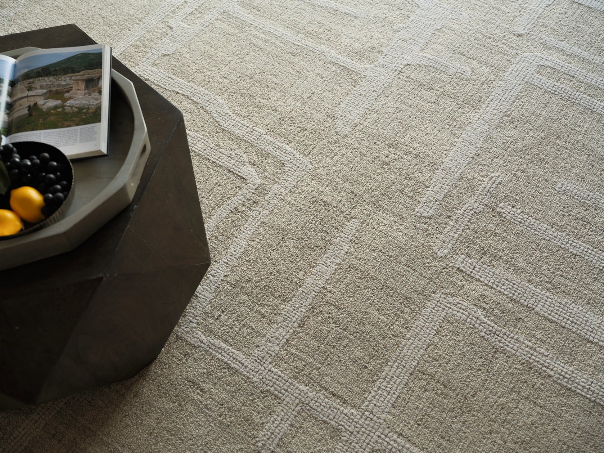 Beige textured rug on the floor with a dark coffee table; a light gray tray on the table holds black grapes, yellow lemons, and an open magazine.