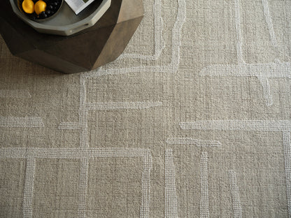 Beige geometric area rug with white rectangular borders; textured loop pile and a dark faceted coffee table in corner.