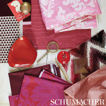 Pink, burgundy and red satin fabric swatches with a red glass bowl, brass ring and candle.