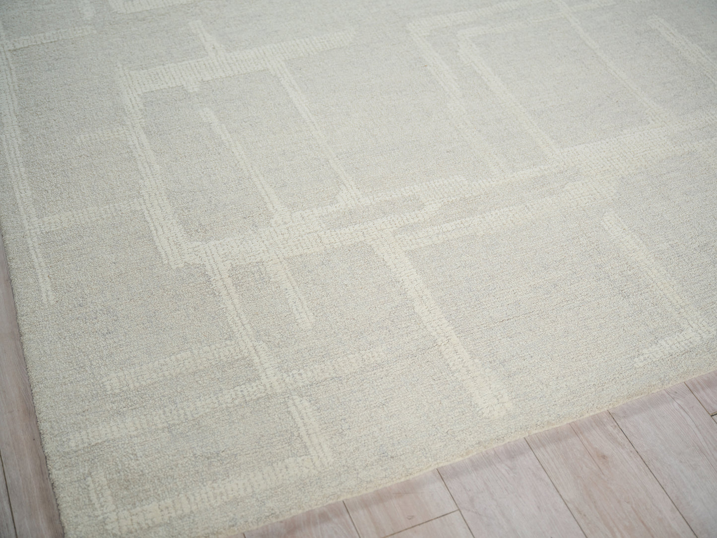 Beige textured area rug with a subtle geometric square pattern on a light wood floor.