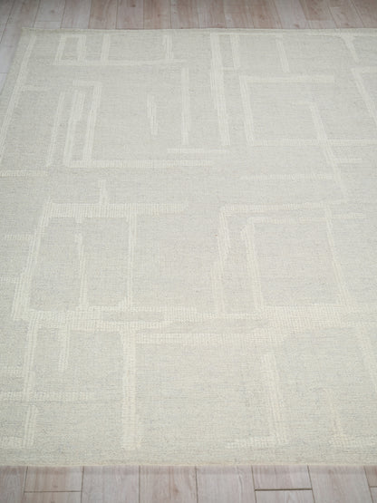 Light beige area rug with a subtle geometric rectangle pattern on a light wood floor, size 6' x 9'.