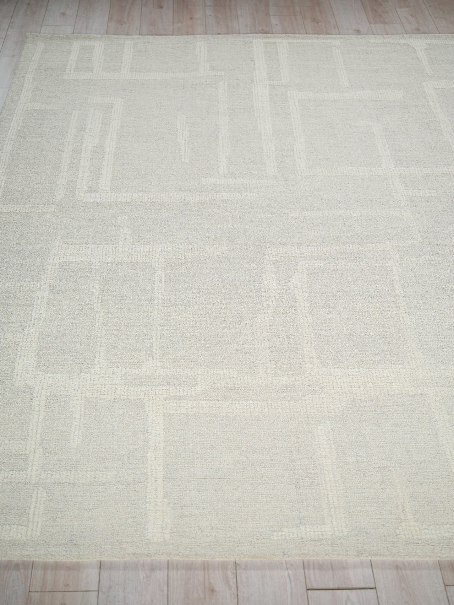 Light beige geometric area rug with pale square patterns and soft woven texture on wood floor