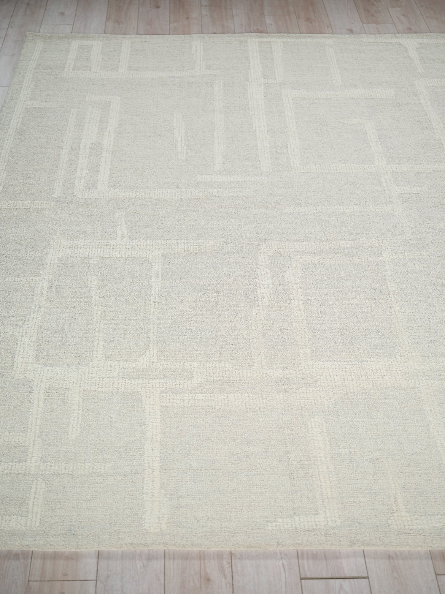 Light beige geometric area rug with pale square patterns and soft woven texture on wood floor