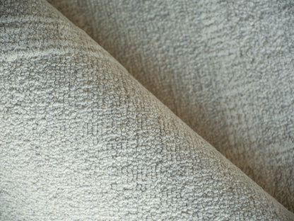 Beige textured boucle fabric close-up on a rug, plush surface with soft nubby pile and folds.