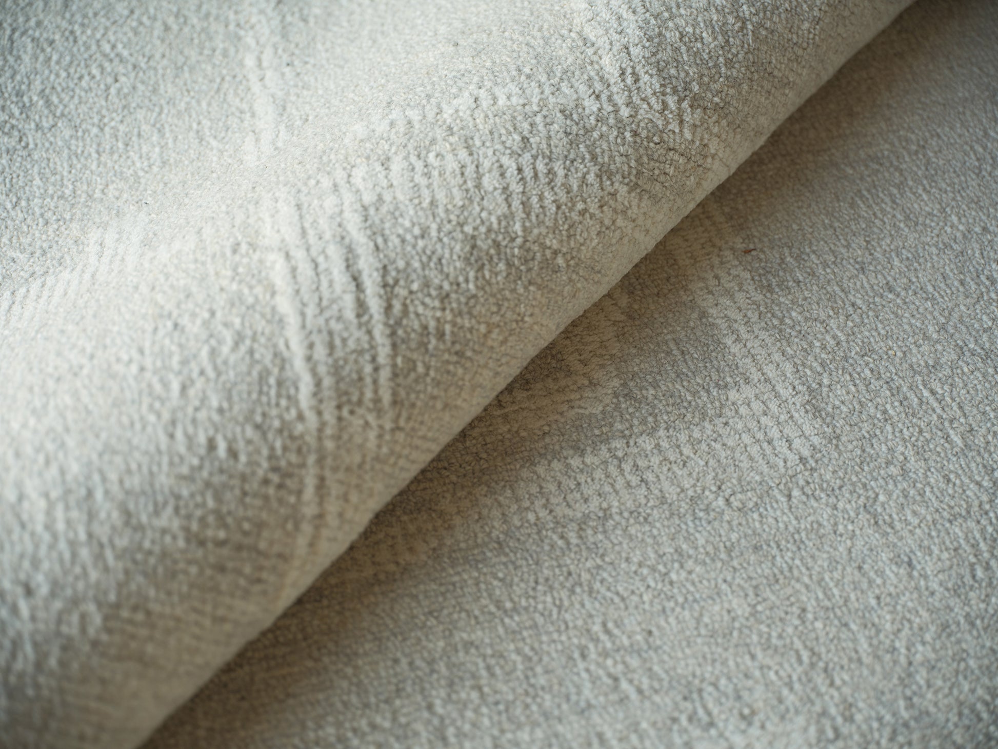 Beige hand-tufted rug close-up of a folded edge with soft looped pile.