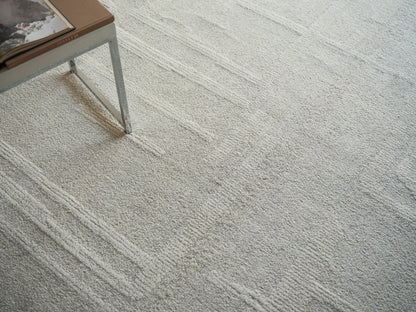 Soft beige textured rug with subtle linear pattern; metal-legged side table and a brown book on top.