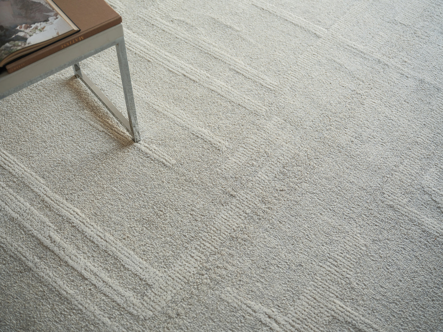 Neutral textured gray-beige rug with a metal-framed side table and a brown hardcover book on top.