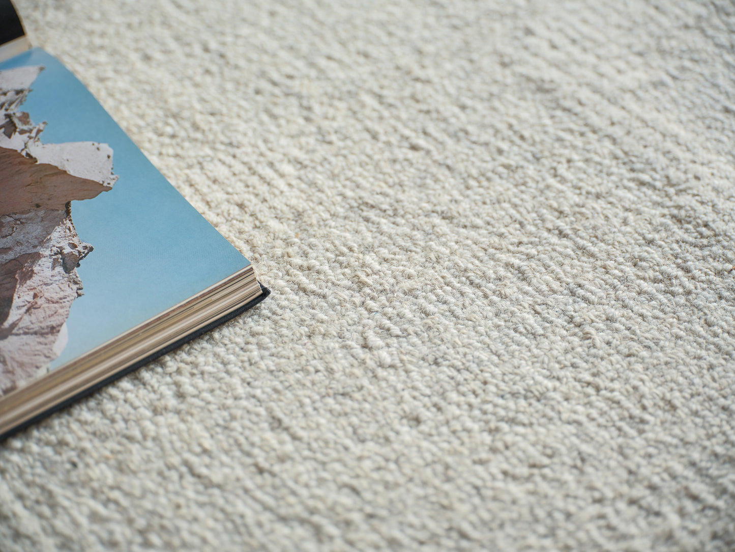 Corner view of a rug on a beige carpet, with a magazine resting nearby.