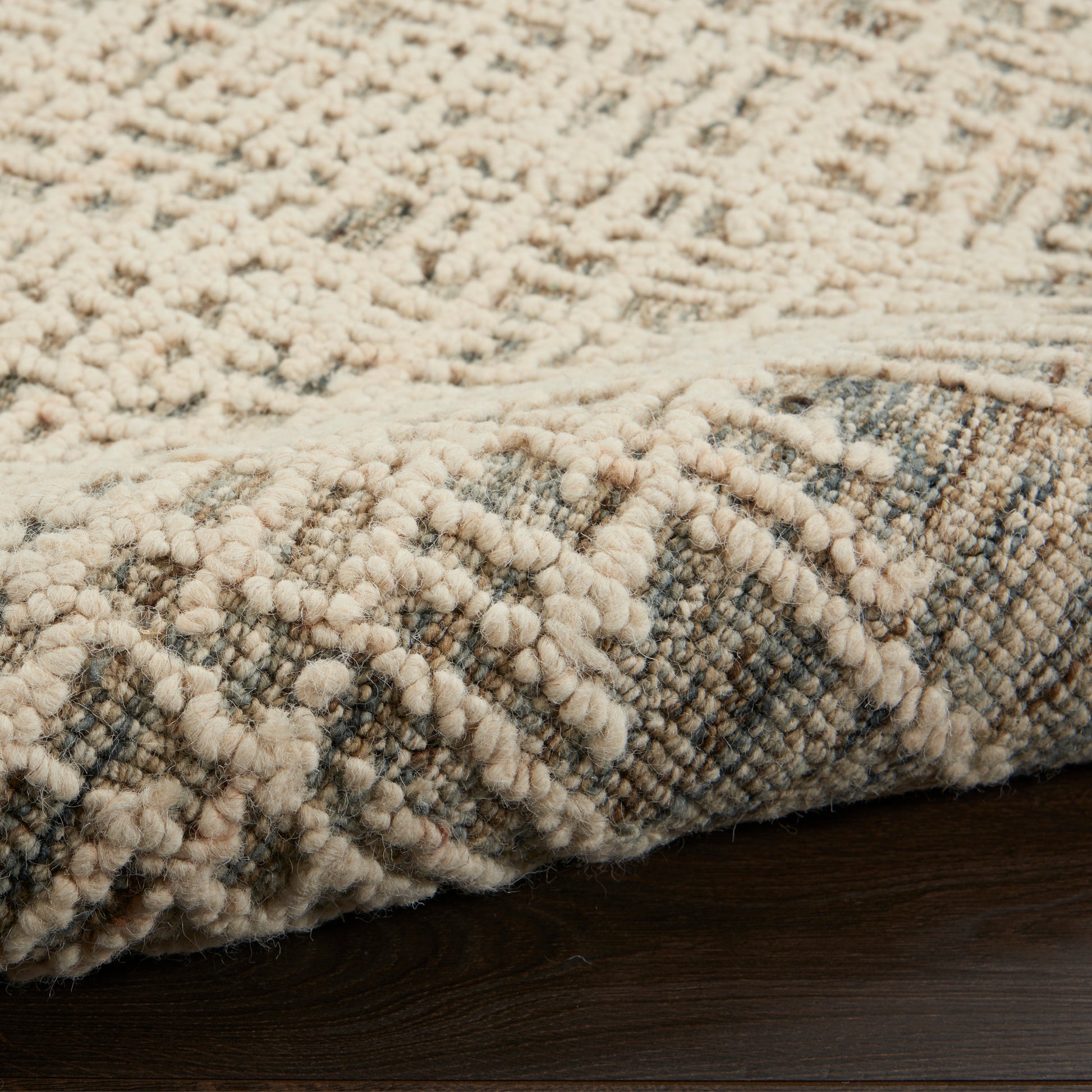 Close-up of a cream boucle rug with chunky raised loops on a blue-gray patterned base.