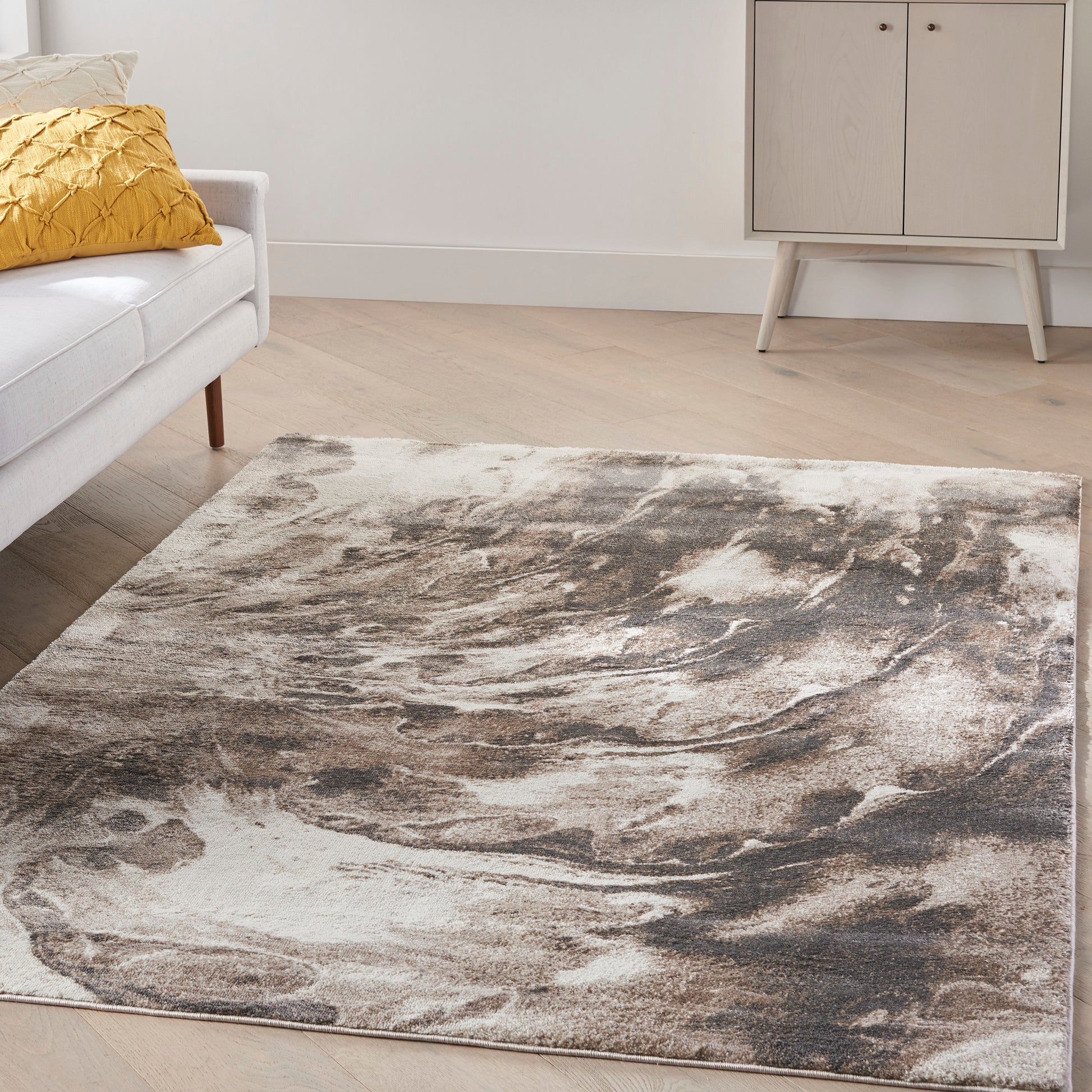 Rectangular plush area rug with abstract taupe, brown and cream swirls in a modern living room on light wood floor.